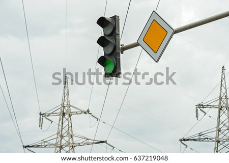 Traffic light with the sign of the main road against the background of high-voltage gear