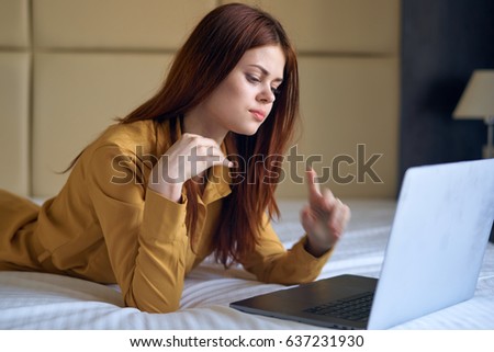   the woman lies on the bed in the orange shirt with the laptop                             