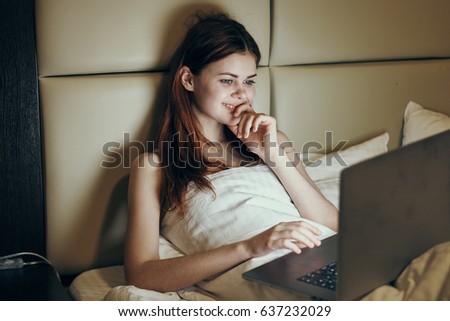  A woman in a dark room smiling looking at laptop                              