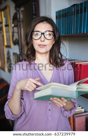 Portrait of a confused mature woman in eyeglasses pointing finger at book and looking at camera