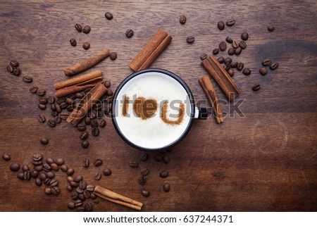 A rustic white mug with coffee cream. Food art creative concept image, I LOVE YOU drawing with cinnamon powder over wooden background.