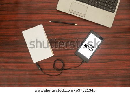 Above view of a book connected to a tablet through an USB cable on a desk. Optical character recognition loading bar.
