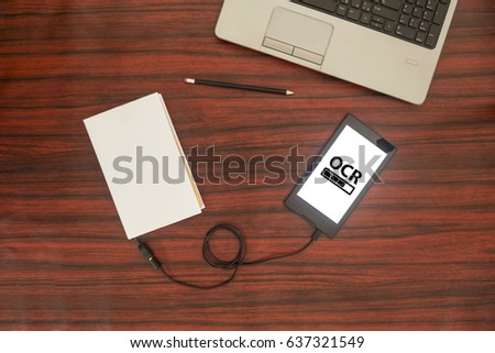 Above view of a book connected to a tablet through an USB cable on a desk. Optical character recognition loading bar.