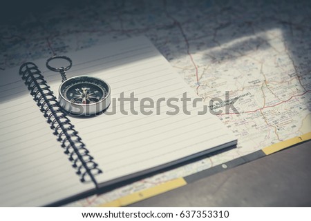 A compass with a pen on notebook and using a map to navigate