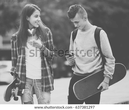 Portrait of cheerful teenager couple with skateboards and smartphones outdoors 
