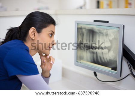 Closeup portrait of allied health dental professional in blue scrubs examining dental x-ray on computer screen, isolated dentist office Royalty-Free Stock Photo #637390948