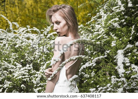 Blond girl in white dress among white flowers. Spring