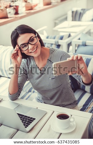 Young beautiful business lady sitting in a cafe drinking coffee and using a telephone to make selfie