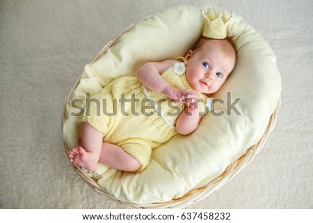 Portrait of newborn baby girl lying in a basket with golden crown and yellow bodysuit Royalty-Free Stock Photo #637458232