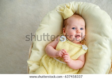 Portrait of newborn baby girl lying in a basket with golden crown and yellow bodysuit Royalty-Free Stock Photo #637458337