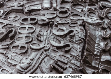 Gray letters on a dark background. Jumbled arrangement of different sized metal letters of the alphabet. Raised metallic signs. Grey black raised Greek letters in perspective. Filled full frame image.