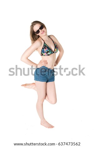 Young, pretty teenager standing with blue shorts and colorful bikini top. studio shot on pure isolated white background