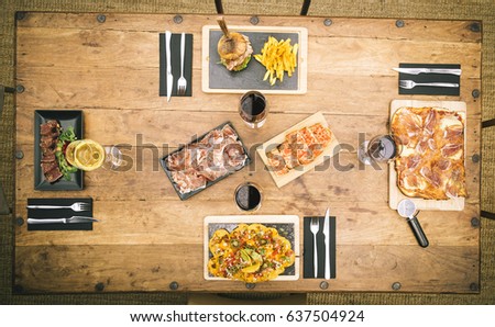 Zenith view of rustic table with nachos, traditional ham pizza, chips and burger, tuna tataki and a plate of Iberian ham