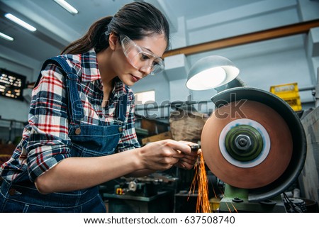 concentrated components factory female staff wearing safety goggles grinding steel product with abrasive disc and flying sparks in milling machine working area. Royalty-Free Stock Photo #637508740