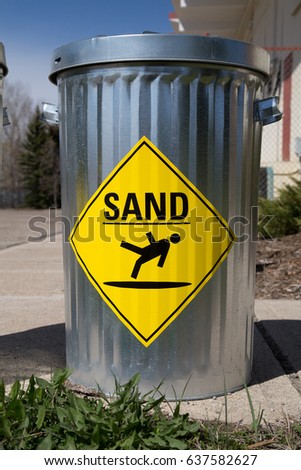 a container of sand used for icy sidewalks, with the bright yellow and black symbol of person slipping 