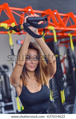 Portrait of athletic slim female fitness model in colorful sportswear exercising with trx suspension strips in a gym club.