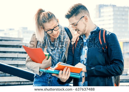 Student couple holding books, in front of their campus.