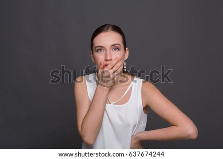 Shocking news. Scared woman covering mouth with hands while posing to camera on gray studio background.
