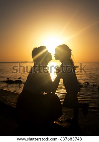 Mother and daughter on the beach during sunset. Back-light. Ray of sun.