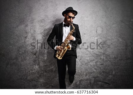 Jazz musician playing a saxophone and leaning against a rusty gray wall Royalty-Free Stock Photo #637716304
