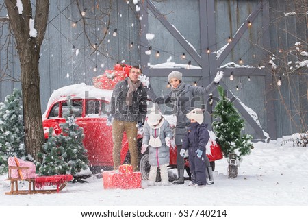 Snowy day, Christmas decorations. Happy family (mom, dad, son and daughter) playing snowballs on a red car background.