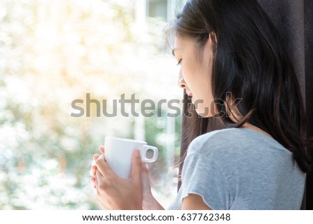 Portrait of a happy asian woman thinking and holding coffee cup