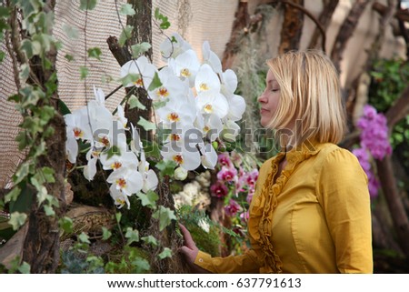 A young woman is standing in the middle of a nice park and she is smelling white orchids.