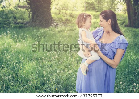 Pregnant mother playing with little daughter in park. Mother and daughter in meadow.