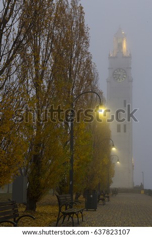 Alley lined with benches, street lamps and poplar trees in the mist with the 45-metre Clock Tower in the background, Old Port of Montreal, Quebec, Canada