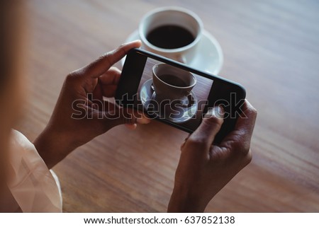 Hands of woman taking a clicking picture of black coffee in restaurant