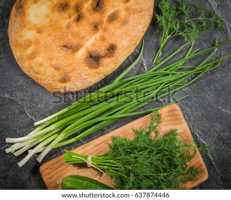 A large loaf of bread with green onions and dill on a black background. View from above.