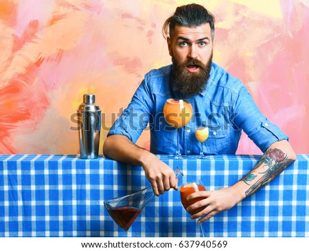 Bearded man, long beard. Brutal caucasian surprised hipster with moustache in denim shirt doing cocktails and alcohol shot with bar stuff on blue checkered plaid on colorful texture background