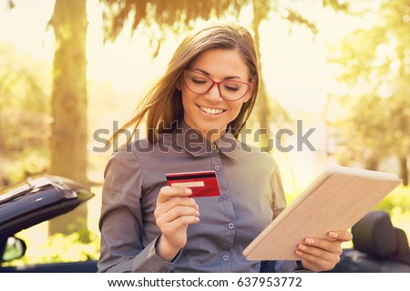 Smiling woman standing by her new car making online payment on her tablet computer outside on a sunny summer day   Royalty-Free Stock Photo #637953772