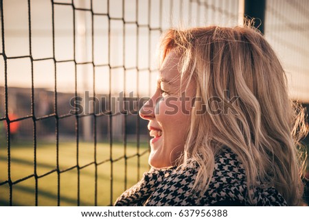 Young pretty blond hair smiling woman - football fan portrait. Aunt cheers for her nephew playing soccer on local green field. Parents picking up kids from their after school activities - concept Royalty-Free Stock Photo #637956388