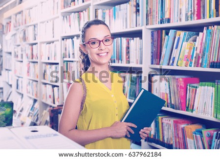 Young cheerful woman buying books in hard cover in bookstore