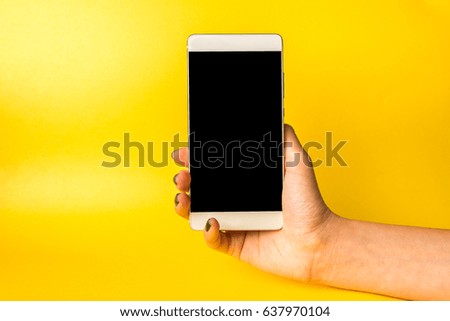 Woman hand holding smartphone on yellow background.