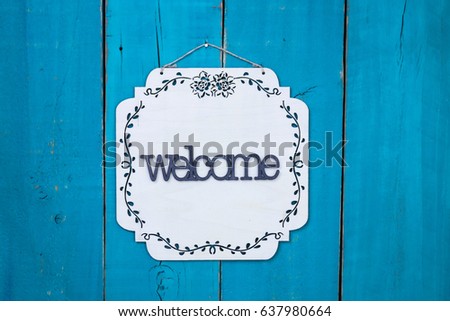 Welcome sign with floral border hanging on antique rustic teal blue wood door; family, home, love concept background with painted copy space