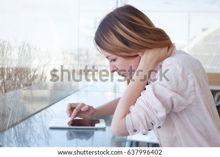 young woman using digital tablet gadget in modern interior, checking email and social networks online