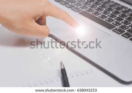 motion image of a hand that is going to click on something on the laptop. Laptop, pen and paper as a background. Brightness on the tip of the finger.