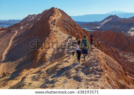 Focus on backpackers / tourists walking on rock formations in the Atacama desert with a slightly blurred background, Chile.