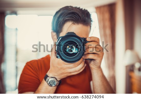 Young man photographer making selfie at mirror. Focus on camera lens.