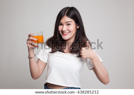 Young Asian woman thumbs up drink orange juice on gray background