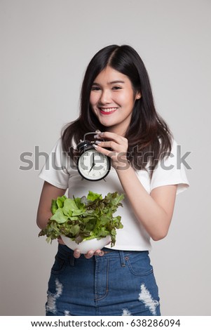 Young Asian woman with clock and salad on gray background