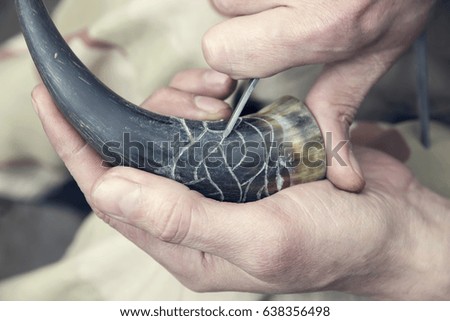 Hands of a craftsman who cut out with the help of a special tool patterns in the horn. Close Up.