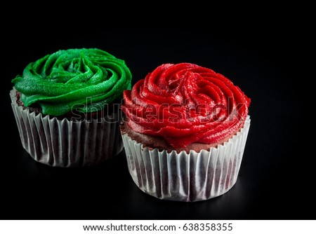 Two cupcakes, frosted in swirled red and green and isolated on black  background