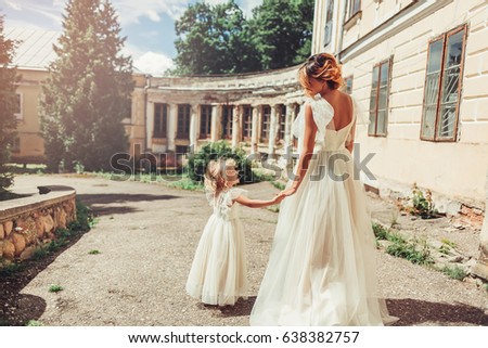 Stylish mom with her daughter in beautiful elegant long light dresses walking outdoors