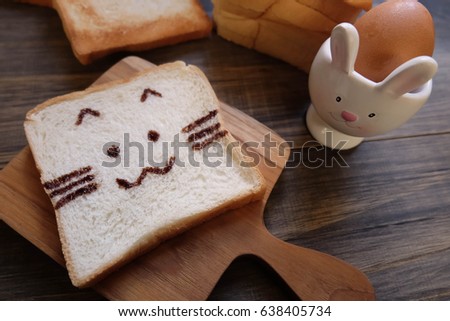 Bread decorated with chocolate is a cat image on a wooden tray with scallion eggs.Good morning concept