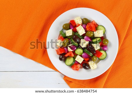 delicious Greek salad with fresh vegetables, feta cheese green and kalamata olives, red onion bulbs on white plate on table mat, easy and healthy recipe,view from above