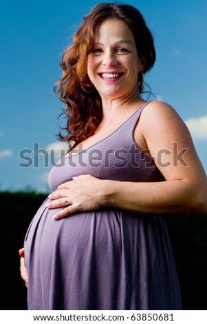 Young pregnant woman stand in grass. Beautiful and happy model.