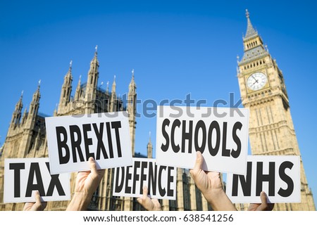 Hands holding election signs protesting modern British social issues like Brexit, tax, education, defense, and health in front of the Houses of Parliament at Westminster Palace, London, United Kingdom